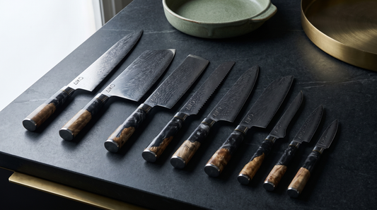 Aiko Black Damascus knives with black resin handles fanned out on a charcoal soapstone worktop